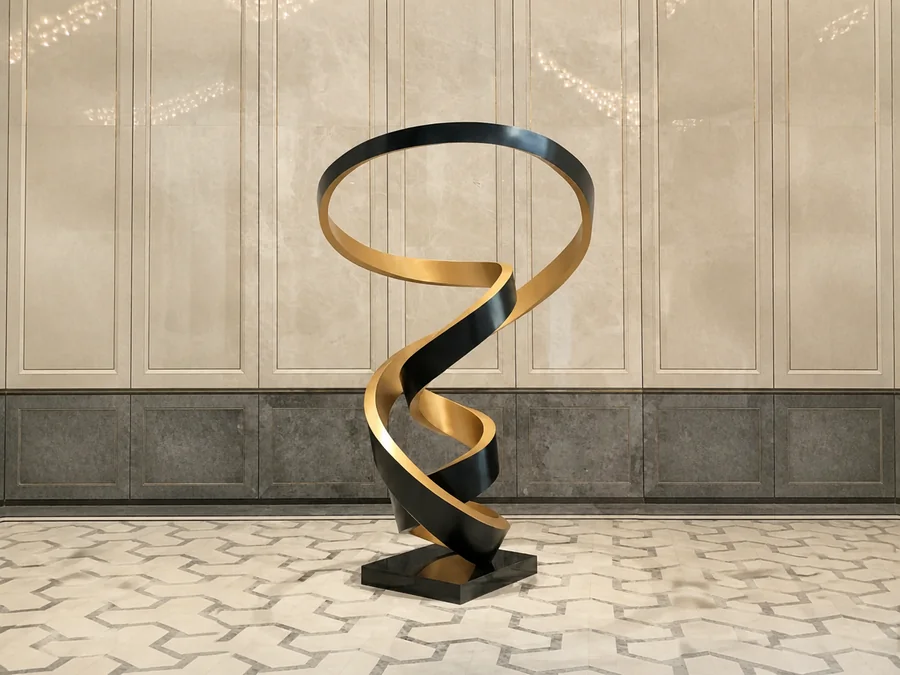 Black and gold spiral stainless steel sculpture displayed in a corporate office lobby