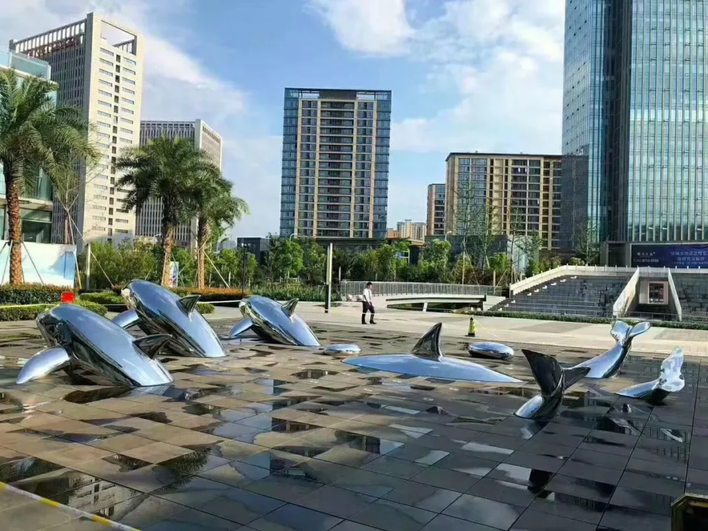 Polished stainless steel dolphin sculpture installation in a modern commercial plaza