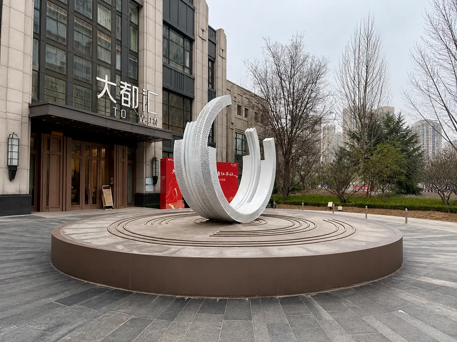 White perforated stainless steel open ring sculpture installed at a commercial plaza entrance