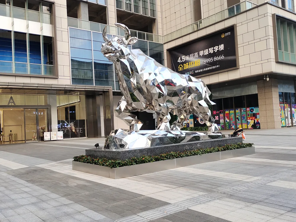 Faceted mirror-polished stainless steel bull animal sculpture in a commercial plaza