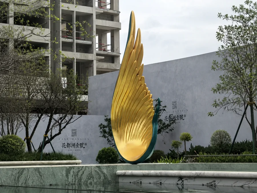 Large gold stainless steel wing sculpture installed at a luxury private estate entrance