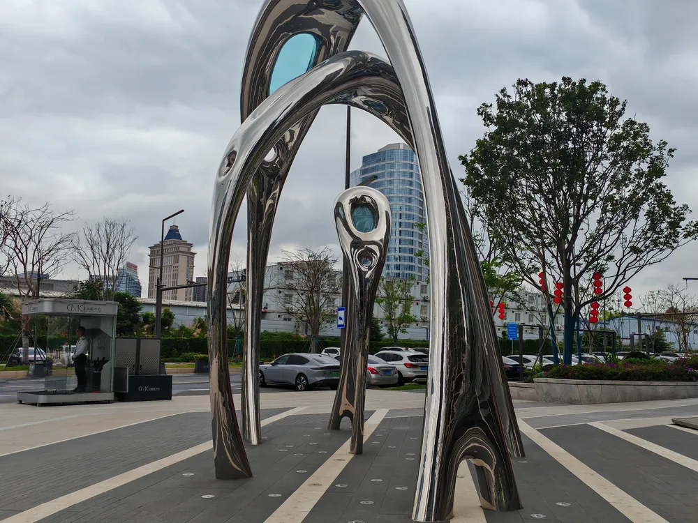 Mirror-polished stainless steel geometric arch sculpture installed in a public plaza