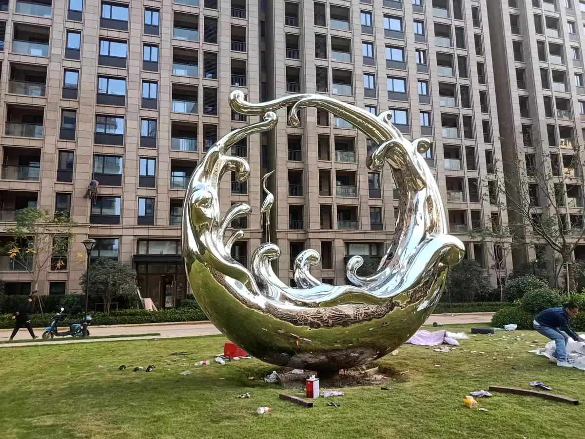 Mirror polished stainless steel wave sculpture installed in an outdoor residential landscape