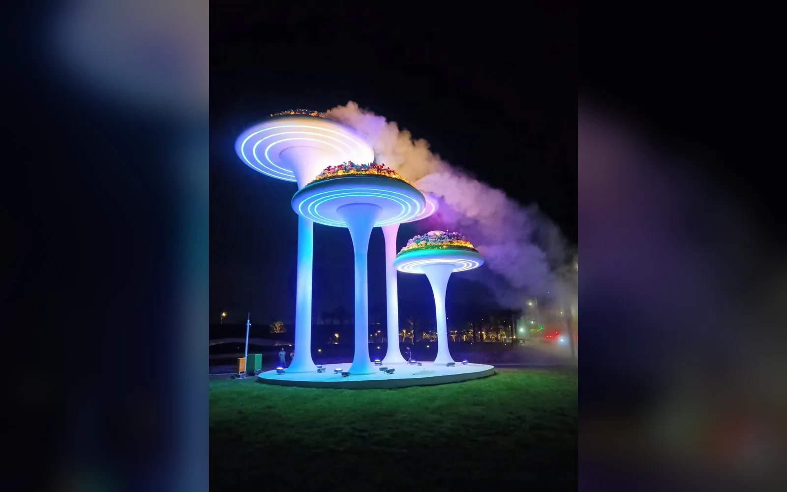 Illuminated stainless steel mushroom landscape sculpture with mist in a garden at night