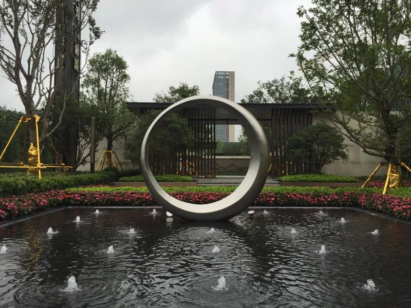 Stainless steel circular water feature sculpture installed in a landscaped garden